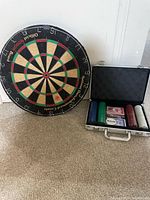 Photo showing one round dartboard and open poker set metal carrying case containing poker chips, two decks of cards and a dealer button.