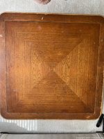 Top view of square coffee table showing medium brown wood finish with diamond pattern grain and surface scratches.