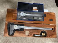 Top view of two wooden cases containing dial calipers, micrometer, height gauge, and gauge blocks with foam padding