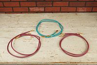 Three Tara Labs audiophile interconnect cables displayed on wooden surface, two purple Prism 33 cables and one turquoise Prism 22 cable each approx 1 meter, gold-plated RCA connectors visible.