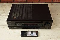 Front and top angle view of black Denon AVR-1000 AV receiver with remote placed in front showing the unit's vents and main controls.