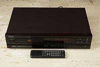 Front and top view of black Denon DCD-590 CD player with remote control placed on white surface.