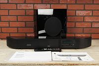 Denon DHT-FS3 soundbar with subwoofer and remote control, manuals on table in front of brick wall.