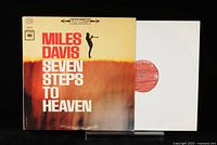 Front cover of the Miles Davis 'Seven Steps to Heaven' vinyl album with the record partially visible in a white protective sleeve.