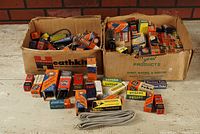 Full view of two cardboard boxes filled with vintage radio vacuum tubes in original colorful boxes plus some loose tubes and a coiled gray cable