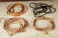 Lot of various speaker cables on a wooden table, some with banana plug connectors, transparent insulation showing copper wiring inside.
