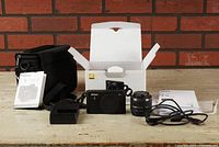 Full view of Nikon 1 J2 camera, Nikkor 10-30mm zoom lens, battery charger, USB cable, manuals, camera bag and open box.