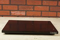 Front angle showing the rectangular dark wood platform with Mission logo on front right corner and round feet beneath.