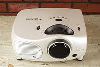 Front angled view of white Optoma HD7100 home theater projector showing lens, vents, and control buttons on top.