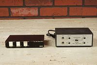 Photo showing both QED M.C. Pre-Amplifier and Realistic External Phono Stage side by side on a wood surface with brick wall background.