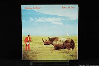Front cover of Adrian Belew Lone Rhino vinyl LP showing a man in red suit with a guitar and a rhinoceros in a field with blue sky