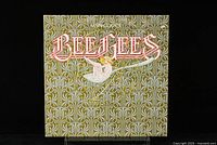 Front cover of Bee Gees Main Course vinyl LP showing ornate green and white pattern background with red Bee Gees logo and angel playing trumpet