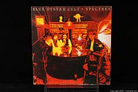 Front cover of the Blue Oyster Cult 'Spectres' LP showing band members seated around a table in a library setting with warm lighting tones.