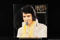 Front cover of Elvis - A Canadian Tribute LP showing Elvis Presley holding a yellow microphone in a white sequined outfit and yellow scarf.