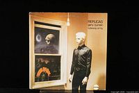 Front cover of 'Replicas' vinyl LP showing Gary Numan figure near a window.