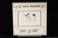 Front cover of Love and Rockets Earth, Sun and Moon LP showing white background with band photo taped on and handwritten title.