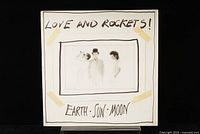 Front cover of 'Love and Rockets Earth Sun and Moon' LP showing the band members and handwritten style text.