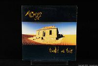 Front cover of Midnight Oil Diesel And Dust album featuring an abandoned house in a desert landscape with band and album name in yellow text.