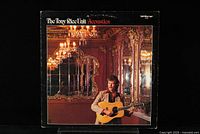Front cover of The Tony Rice Unit 'Acoustics' vinyl LP with Tony Rice holding a guitar in an ornate room with mirrors and chandeliers.
