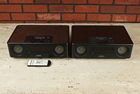 Two Yamaha TSX-130 desktop audio systems with real wood tops and black front panels, placed side by side on a white surface with brick background, along with one remote control in front.