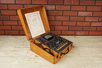 Angled view of the open tube tester inside its wooden carrying case, showing control panel, meter, tube sockets, and attached cord