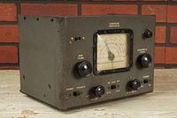 Front angled view showing the radio's metal casing, large tuning dials, analog frequency meter, multiple switches, and volume knob.