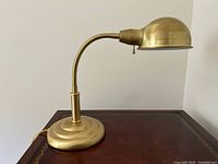 Vintage brass adjustable desk lamp with round weighted base and dome shade, shown fully upright on brown surface.