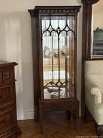 Front view of tall wooden curio cabinet with glass door and mirrored back showing interior shelves