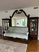 Full view of arched mahogany mirror hung on wall above green upholstered settee with side cabinets flanking.