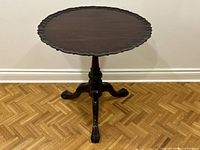Front view of the dark wood antique style round table showing scalloped edges and clawfoot tripod base.