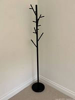 Full view of the black metal coat rack showing upright cylindrical main post with multiple angled tubular branches and round base.