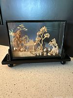 Front and side angle showing the carved wood scene inside glass case with black base