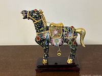 Front and side view of black cloisonné horse decorated with floral designs, gold accents, and mounted on wooden base.