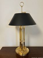 Full view of the brass candlestick style table lamp with black lampshade on a wooden surface, showing height and design.