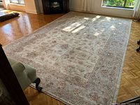 View showing full rug on parquet floor with light beige and taupe floral pattern and border.