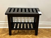 Dark stained wooden hallway bench with slatted top and shelf underneath shown from front on hardwood floor.