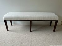 Front view of modern upholstered bench showing cream textured fabric and dark wooden legs.