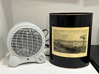 Photo of white space heater/fan beside black metal waste paper bin with Fredericton engraving.