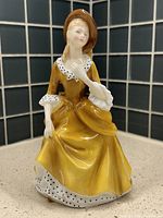 Front angled view of Royal Doulton Sandra figurine in yellow dress showing face, upper body, and seated posture.