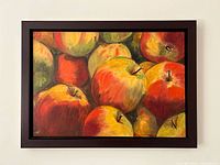 Front view of still life artwork showing red and golden apples in a dark wood frame hung on a white wall.