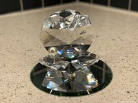 Crystal oyster sculpture with hinged opening, showing pearl inside, resting on round mirror base.