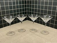 Four Tiffany & Co crystal martini glasses with etched Plaid pattern, shown from front against tiled corner background.