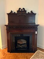Front view of the Victorian-style mahogany mantelpiece and electric fireplace insert showing ornate carved floral appliqué and black marble surround.