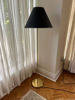 Full height view of the vintage brass floor lamp standing on hardwood floor next to sheer curtains letting in daylight.