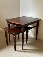 Two vintage mahogany nesting tables stacked with the smaller table underneath the larger one, both with tapered fluted legs.