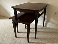 Front view of two nested vintage mahogany side tables with leather tops and detailed legs.