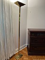 Full view of the standing brass floor lamp showing its height and base near curtain and wooden furniture