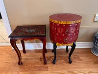 Both red accent tables shown front view, square table left with floral top, round table right with drawers and decorative motifs