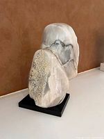 Side view showing natural veining and textured surface of the marble sculpture mounted on a black base.