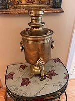 Front view of brass samovar on table, showing body, spigot, and pedestal base.